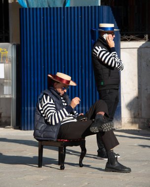 Gondoliere Canale Grande 'de takılıyor ve misafirleri beklerken eğleniyor.