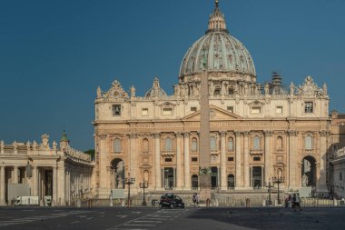 Sabahın erken saatlerinde güneş ışığı Basilica di San Pietro 'nun muhteşem yüzünü aydınlatıyor ve Bernini' nin Vatikan, Roma, İtalya 'daki St. Peter Meydanı' na bakan anıtsal sütununu..