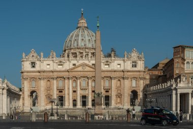 Sabahın erken saatlerinde güneş ışığı Basilica di San Pietro 'nun muhteşem yüzünü aydınlatıyor ve Bernini' nin Vatikan, Roma, İtalya 'daki St. Peter Meydanı' na bakan anıtsal sütununu..
