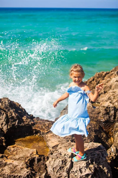 Little girl standing on rocks near sea with waves on background — Stock Photo, Image