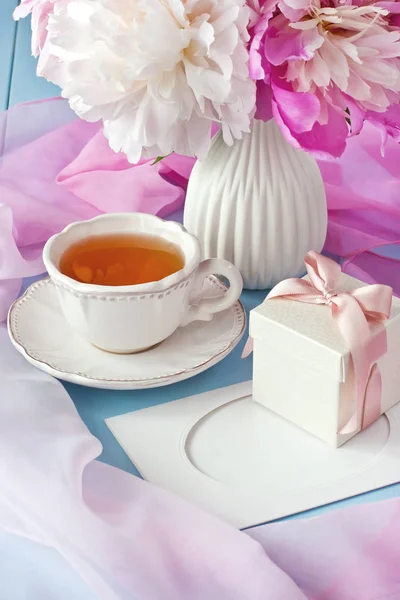 Peonies flowers in vase and cup of tea — Stock Photo, Image