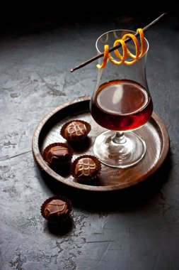 Portakal kabuğuyla süslenmiş tatlı likörlü kompozisyon koyu masa üzerinde çikolata şekerlemeleri, seçici odak