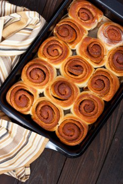 Ev yapımı puf puf böreği tarçınlı rulo fırın tepsisi üzerinde eski, siyah ahşap arka planda. Düz yatıyordu