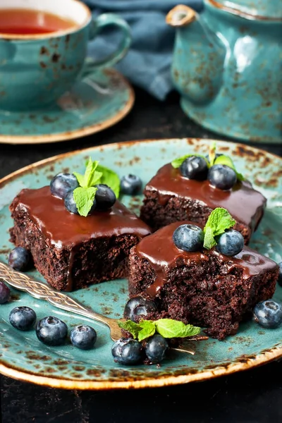 Yaban mersinli çikolatalı kek ve koyu beton arkaplanlı çaydanlıklı çay fincanı, sığ alan derinliğinde seçici odak