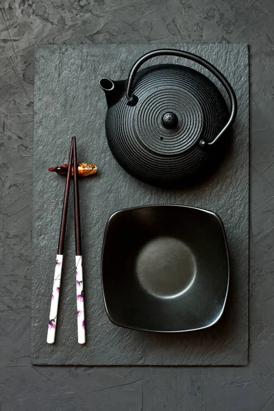 Black slate plate with chopstick on dark background. Flat lay. Asian food concept