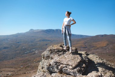 Sırt çantalı bir kız dağlarda bir kayanın üzerinde oturur ve doğanın tadını çıkarır..