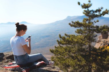 Genç kız telefona bakıyor. Dağların ve doğanın güzel manzarası. 