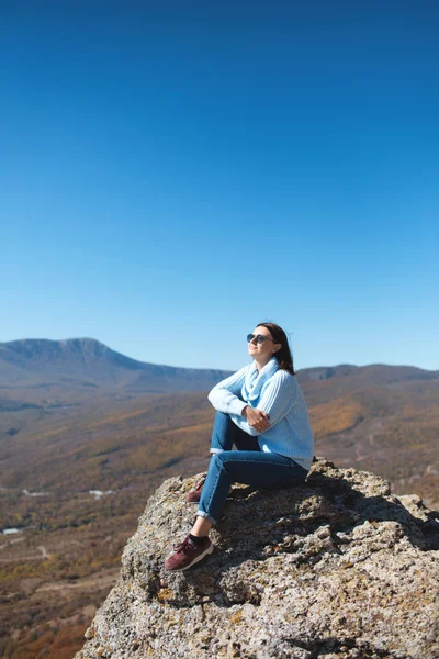 Una chica se sienta en una roca en las montañas y disfruta de la vista de la naturaleza . — Foto de Stock