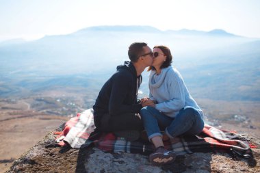A loving couple with a backpack sits on a rock in the mountains and enjoying view of nature.