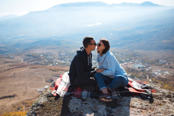 A loving couple with a backpack sits on a rock in the mountains and enjoying view of nature.