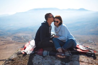 A loving couple with a backpack sits on a rock in the mountains and enjoying view of nature.