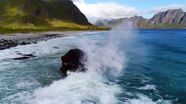 Waves hitting a big rock near the shore near the mountain