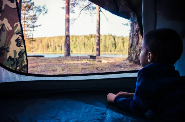 Küçük çocuk göl manzarasında çadıra bakıyor. — Stok fotoğraf