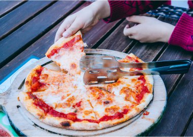 Küçük çocuğun elleri margherita pizzasından bir dilim alıyor.