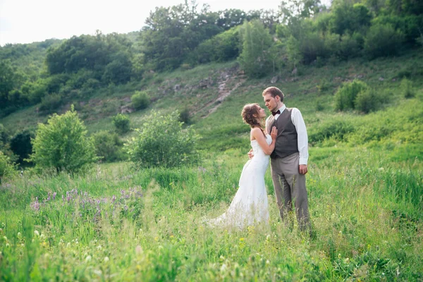 Das Brautpaar mit einem Strauß im Gras vor dem Hintergrund der Berglandschaft — Stockfoto