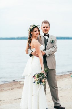 Genç damat ve gelin ayakta nehrin arka plan üzerinde sarılma.