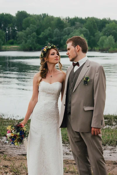 Fiatal vőlegény és menyasszony állandó átölelve a háttérben folyó — Stock Fotó
