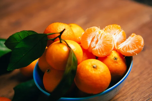 Muchas naranjas frescas de mandarina en un tazón azul, de pie sobre una mesa de madera —  Fotos de Stock