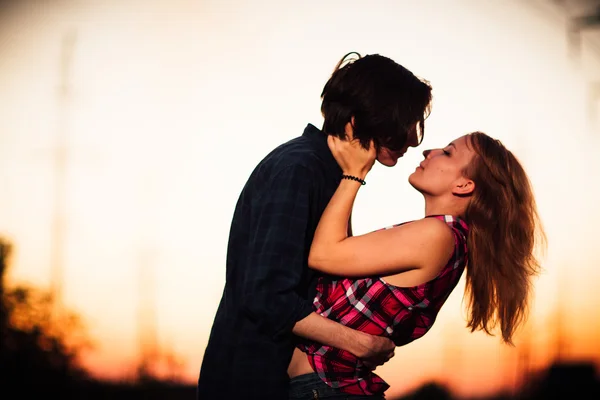 Jongen en het meisje staan zoenen in de zonsondergang achtergrond — Stockfoto