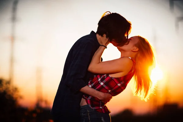 A fickó és a lány állandó a naplemente háttérben csók — Stock Fotó