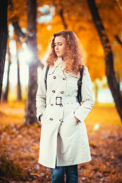 Junges Mädchen im hellen Mantel auf dem Hintergrund des Herbstparks — Stockfoto