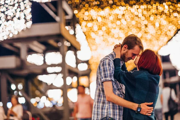 Glückliches Paar, das sich am Abend auf einem Lichterkranz umarmt — Stockfoto