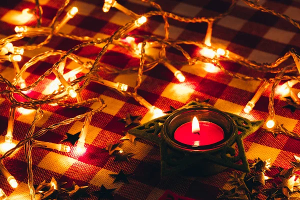 Candle and garland lights in the background of a checkered tablecloth — Stock Photo, Image
