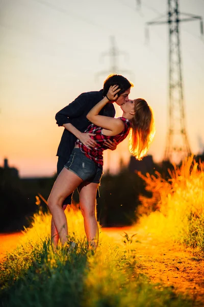 Cara e a menina estão de pé beijando no por do sol fundo — Fotografia de Stock