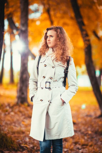 Junges Mädchen im hellen Mantel auf dem Hintergrund des Herbstparks — Stockfoto