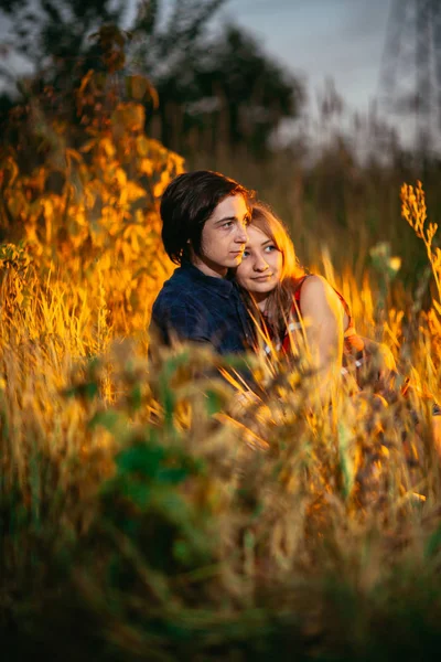 Chlap a dívka sedící v trávě na západ slunce pozadí — Stock fotografie