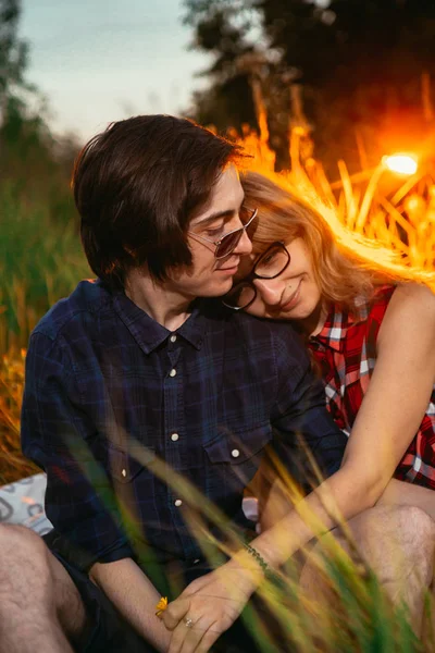 Chico y la chica sentada en la hierba sobre un fondo de puesta de sol —  Fotos de Stock