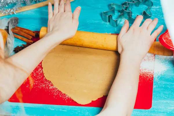 Дівчина закочує тісто на червоній дошці до синього дерев'яного столу — стокове фото