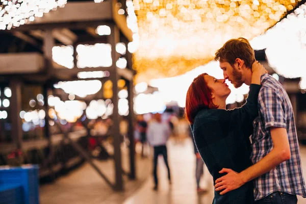 Casal feliz abraçando e beijando à noite em uma grinalda leve — Fotografia de Stock