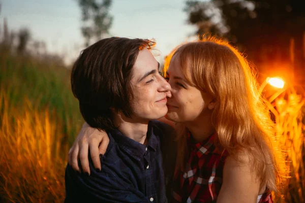 Chico y la chica sentada en la hierba sobre un fondo de puesta de sol —  Fotos de Stock