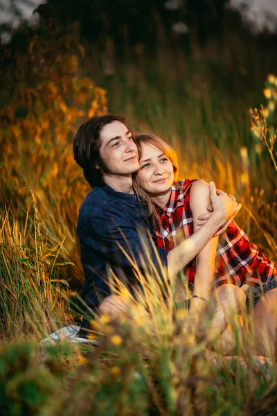 Jongen en het meisje zittend in het gras op een zonsondergang achtergrond — Stockfoto