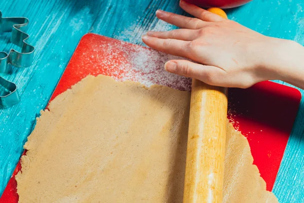 girl rolls the dough on the red board to blue wooden table