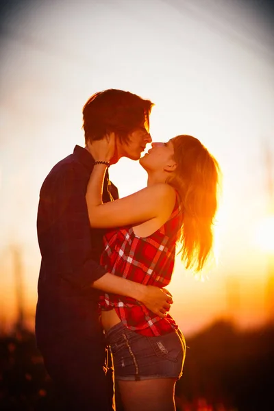 Chico y la chica están de pie besándose en el fondo del atardecer — Foto de Stock