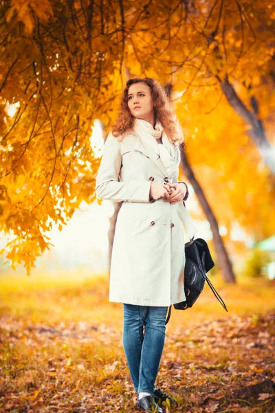 Junges Mädchen im hellen Mantel auf dem Hintergrund des Herbstparks — Stockfoto