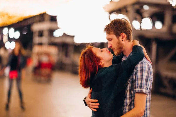 Счастливая пара обнимается и целуется вечером на легких гирляндах — стоковое фото