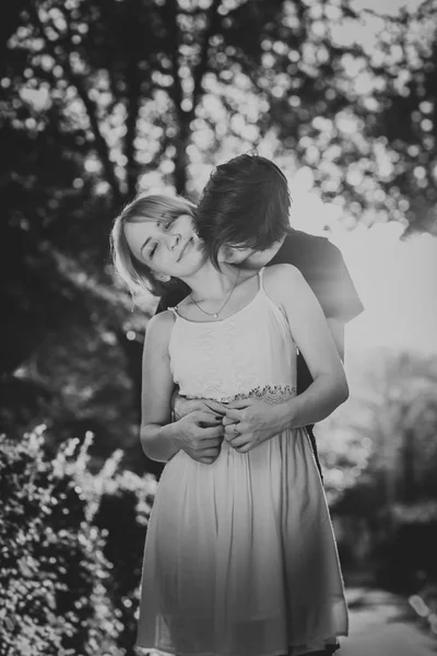Черно-белое фото парня, которого девушка обнимает в фоновом парке — стоковое фото