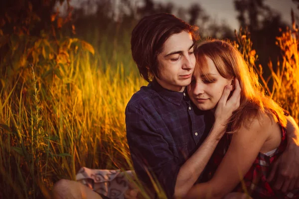 Jongen en het meisje zittend in het gras op een zonsondergang achtergrond — Stockfoto