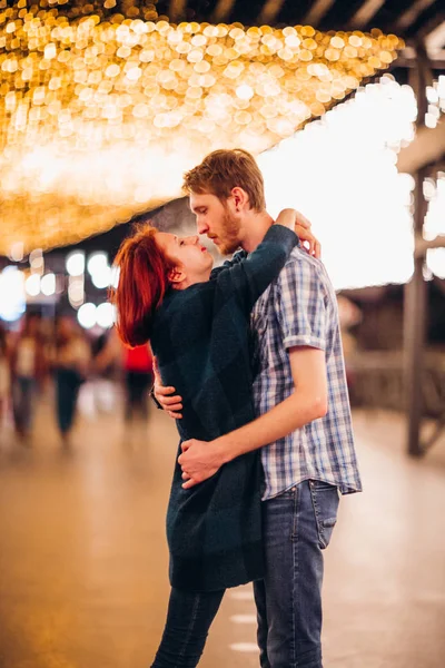 Glückliches Paar, das sich am Abend auf leichten Girlanden umarmt und küsst — Stockfoto