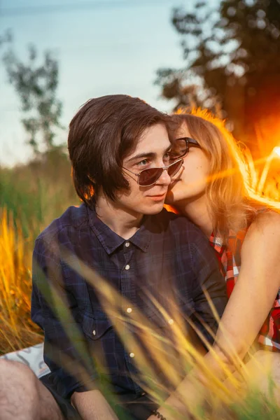 Chico y la chica sentada en la hierba sobre un fondo de puesta de sol —  Fotos de Stock