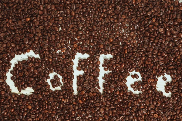 The words coffee written against scattered natural coffee — Stock Photo, Image