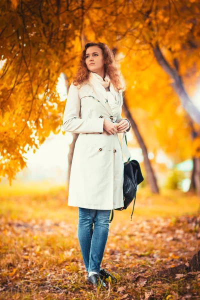 Junges Mädchen im hellen Mantel auf dem Hintergrund des Herbstparks — Stockfoto