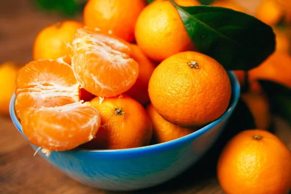 Muchas naranjas frescas de mandarina en un tazón azul, de pie sobre una mesa de madera —  Fotos de Stock