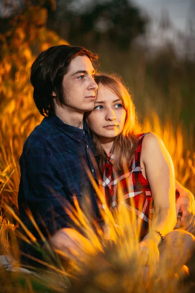 Killen och tjejen sitter i gräset på en solnedgång bakgrund — Stockfoto