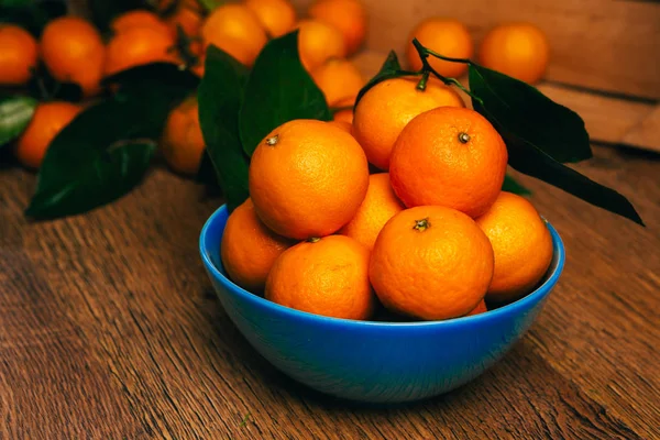 Sok friss mandarin narancs kék tálban, egy fa asztalon áll — Stock Fotó