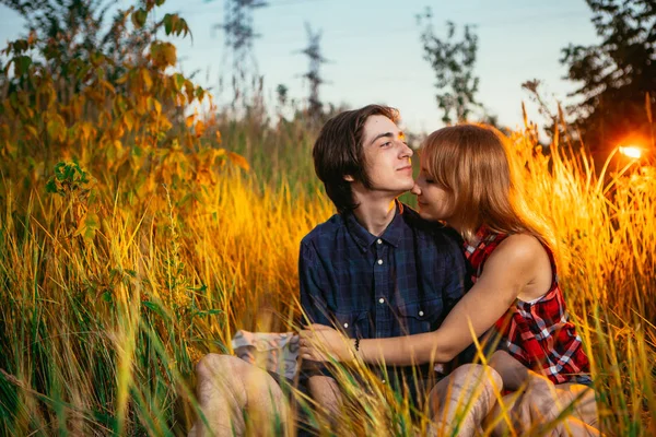 Chlap a dívka sedící v trávě na západ slunce pozadí — Stock fotografie