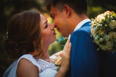 Gelin ve damat, doğa parkında sarılıp öpüşüyor.